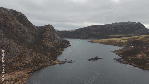 Aerial drone footage showing a mountain lake under cloudy weather conditions. The scene features calm water, surrounding mountainous terrain, and overcast skies, presenting a natural landscape with di