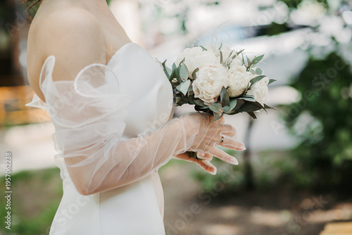The bride holds a bouquet in her hands. The bride's hands are in gloves