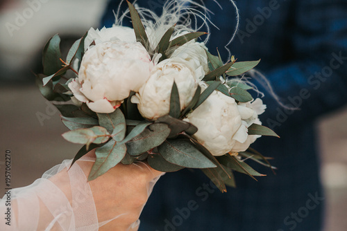 The bride holds a bouquet in her hands. The bride's hands are in gloves
