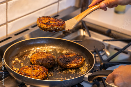 Obraz na plátně Home cook flipping seared burger patties in nonstick skillet on gas stove with w