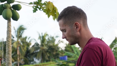 Man eating rambutan with papaya tree in the background