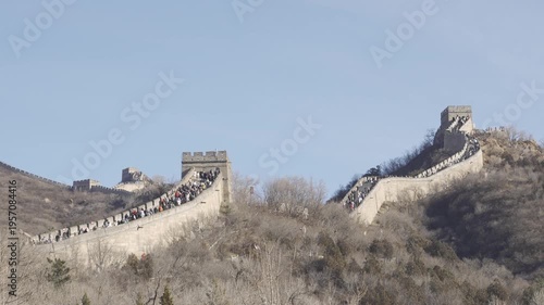 crowded people visit The Great Wall of China among mountain range hill in winter dry winter weather under sunny blue sky, ancient great wall with wide path and crowded people walking on  wall