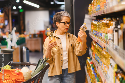 Schilderij op canvas Adult woman comparing cooking oil products in supermarket