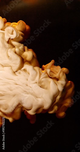 Extreme super slow motion of milk swirling and mixing into coffee, creating smooth creamy clouds and fluid abstract shapes in a dark liquid background. Speed ramp effect. Vertical aspect ratio.