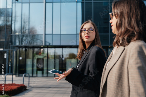Woman walking in city holding tablet while talking to colleague outside modern office building during business hours