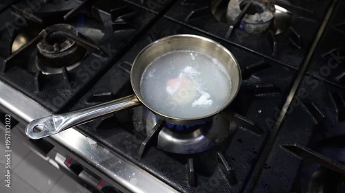 Poaching an egg in a saucepan on a restaurant gas stove