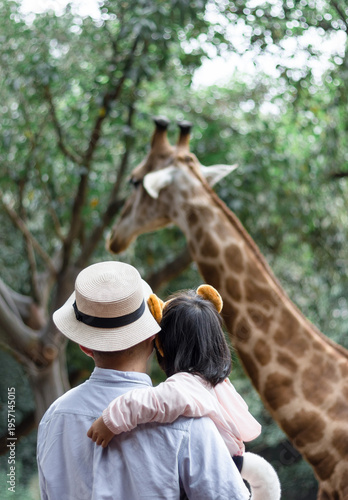 A Chinese father and his daughter visiting the zoo and feeding a giraffe