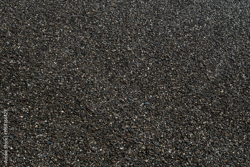 black surface of fine sea pebbles is textured and uneven. Small stones and gravel are embedded in the dark finish. Ideal as a background or design element.