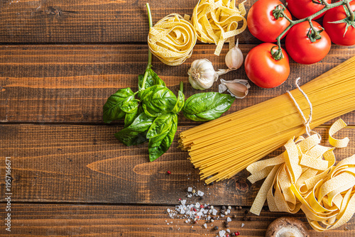 Top view of Italian pasta ingredients on a rustic wooden table. Composition with spaghetti, tagliatelle, fresh tomatoes, basil, garlic, and spices. Traditional Mediterranean cooking concept 