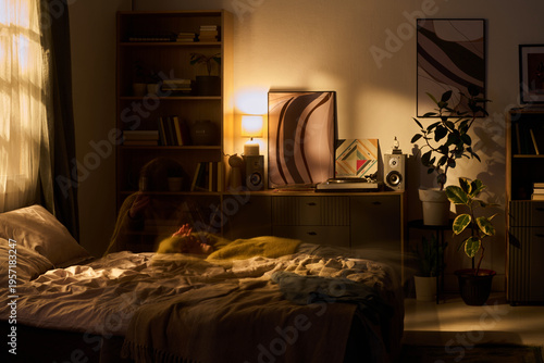 Schilderij op canvas Young woman lying on bed in softly lit bedroom, relaxing with hands behind head,