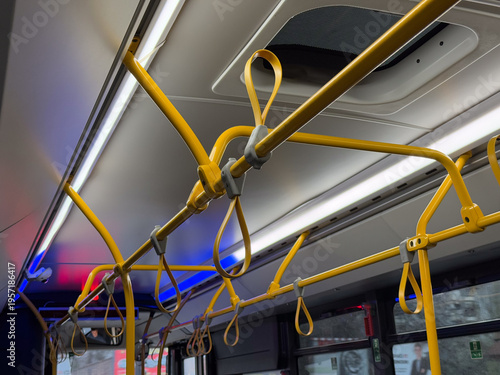 Close view of yellow handrails and hanging handles inside modern city bus. Passenger support system, safety grip design, public transport ergonomics, standing stability, movement control in transit