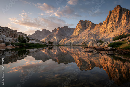 A lake reflecting mountains and a cloudy sky at sunrise or sunset with warm light on the peaks
