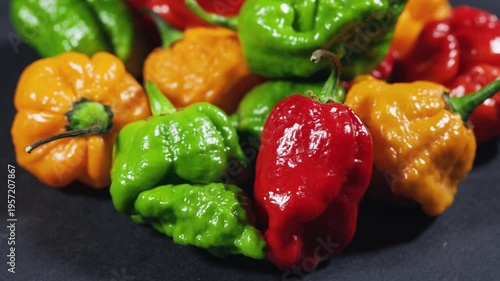 Variety of red, green, orange and yellow hot chili peppers on dark background.