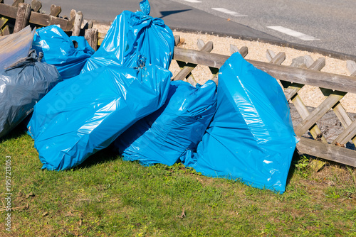 Φωτογραφία Bright blue bags of waste await collection near a wooden fence on a sunny day in