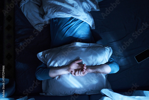 Принти на полотні Adult man lying in bed covering face with pillow, crossing arms over pillow, sma