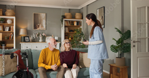 Home health nurse engages with two seniors in their living room. The nurse talks to the couple about their health, while they listen attentively. The living room is bright and welcoming.