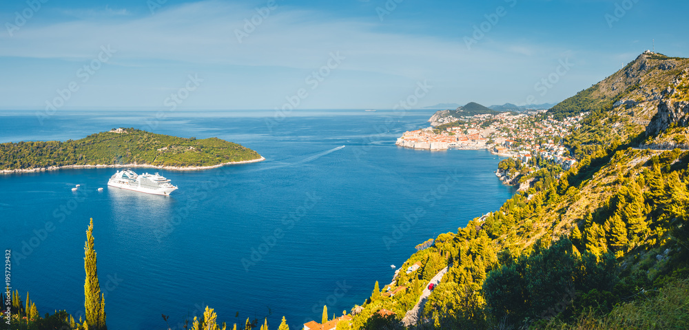 Obraz premium Cruise ship sailing into the stunning turquoise waters of Dubrovnik, with lush hills and historic townscape on a sunny day. Croatia, Dalmatia, Europe.
