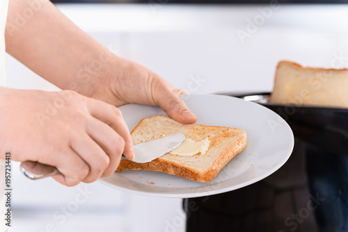 Hand spreading butter on toast on plate, preparing and serving breakfast food, kitchen routine, eating preparation.