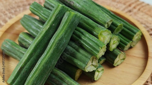 Fresh Moringa pods are arranged on a wooden plate.