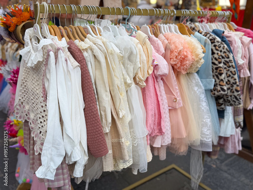 Boutique rack with elegant girls clothing in lace, tulle, and pastel fabrics at a market. Children fashion retail, occasion dressing, curated assortment, and premium textile presentation for festive