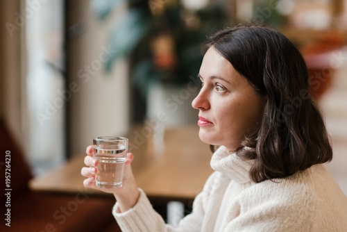 Caucasian woman in her 40s with dark hair wearing white knit sweater working in coworking space using her laptop. Mature female spending time in modern office completing creative or routine tasks.