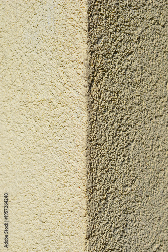 A vertical shot of a building corner showing the contrast between a sunlit light yellow stucco surface and a dark shaded textured wall