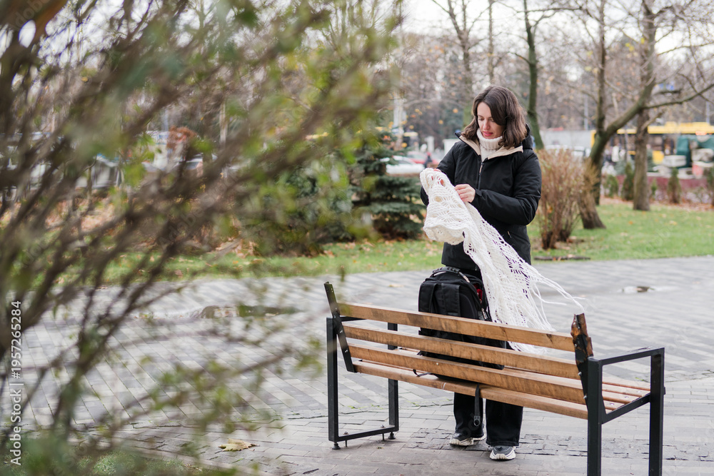Fototapeta premium Caucasian woman in her 40s with dark hair wearing warm clothes walking on the street with her backpack and phone. Mature female spending time outdoors doing her routine tasks and breathing fresh air.