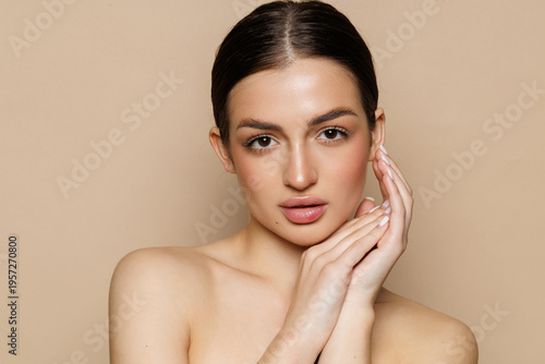 Skin care model. Beautiful young woman with perfect skin touching her face and posing against beige background.