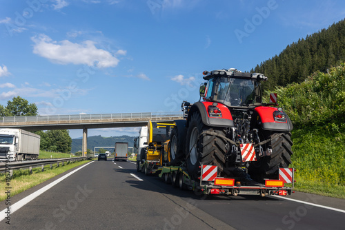 POV heavy industrial truck semi trailer flatbed platform transport big modern farming tractor machine on common alpine highway road bright day sky. Agricultural equipment transportation service work