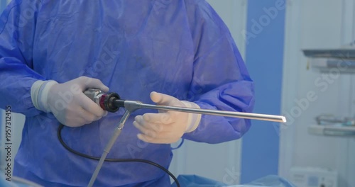 Professional surgeon in sterile blue scrubs holding a long laparoscopic trocar instrument during a minimally invasive surgery.