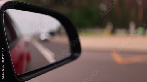 View in the rear view side mirror of a automobile, driving a red car along the road
