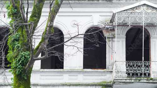 Abandoned building with ornate balcony and overgrown tree in urban setting