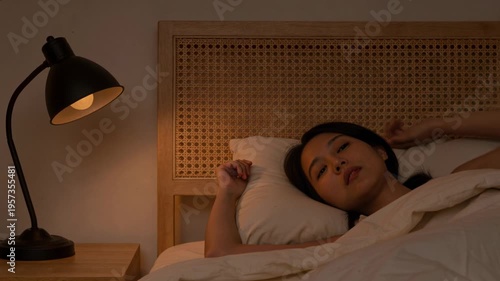 Vertical video: Woman lying in bed seeing glowing lamp reaching turning off and settling for sleep