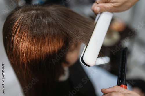 Canvas Print A hairdresser straightens and straightens a client's long, natural dark hair with a flat iron, curling iron, or styler at a salon