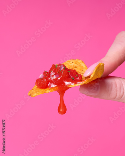 Hand Holding Tortilla Chip with Salsa Dripping on Pink Background
