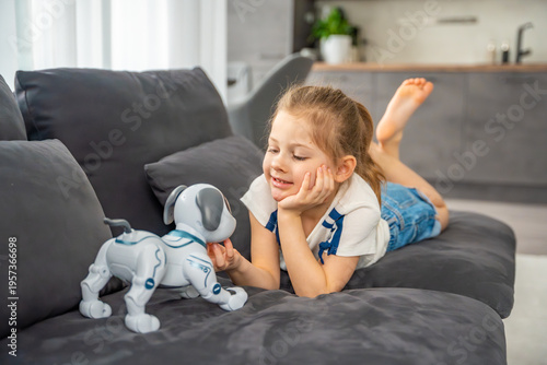 Child hugging robotic dog with affection while sitting on sofa at home. Emotional attachment and digital companionship in modern family life.