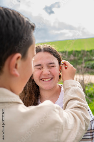 Boy putting daisy flower on sister's ear outdoors