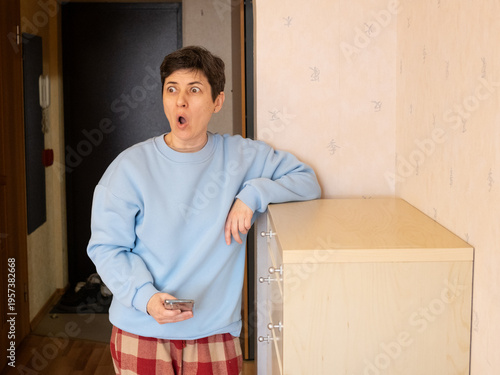 Canvas Print Middle aged woman reacting with surprise and shock while looking at smartphone s