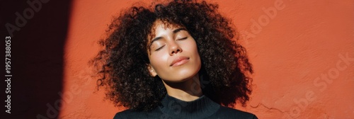 African female young portrait eyes closed basking in sun against textured red wall curly hair peaceful expression