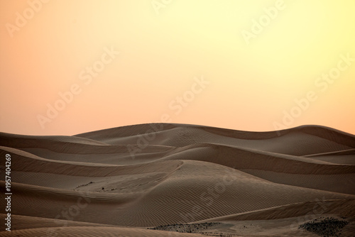 Canvas-taulu Golden sunset light casts soft shadows over rippling sand dunes, creating a serene and vast desert landscape with minimalist appeal