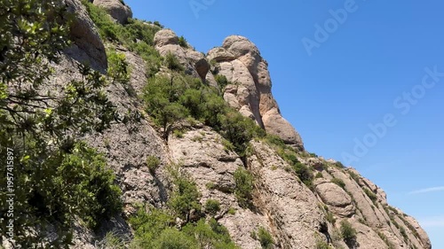 Walking in the mountains of Montserrat in Spain in summer. Panorama of mountain peaks and green plants against the blue sky. Trails for active recreation