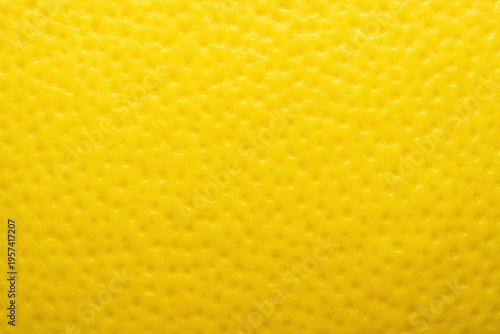 Fruit skin surface made of citrus peel in bright yellow tones with a porous pitted texture in a full frame macro.
