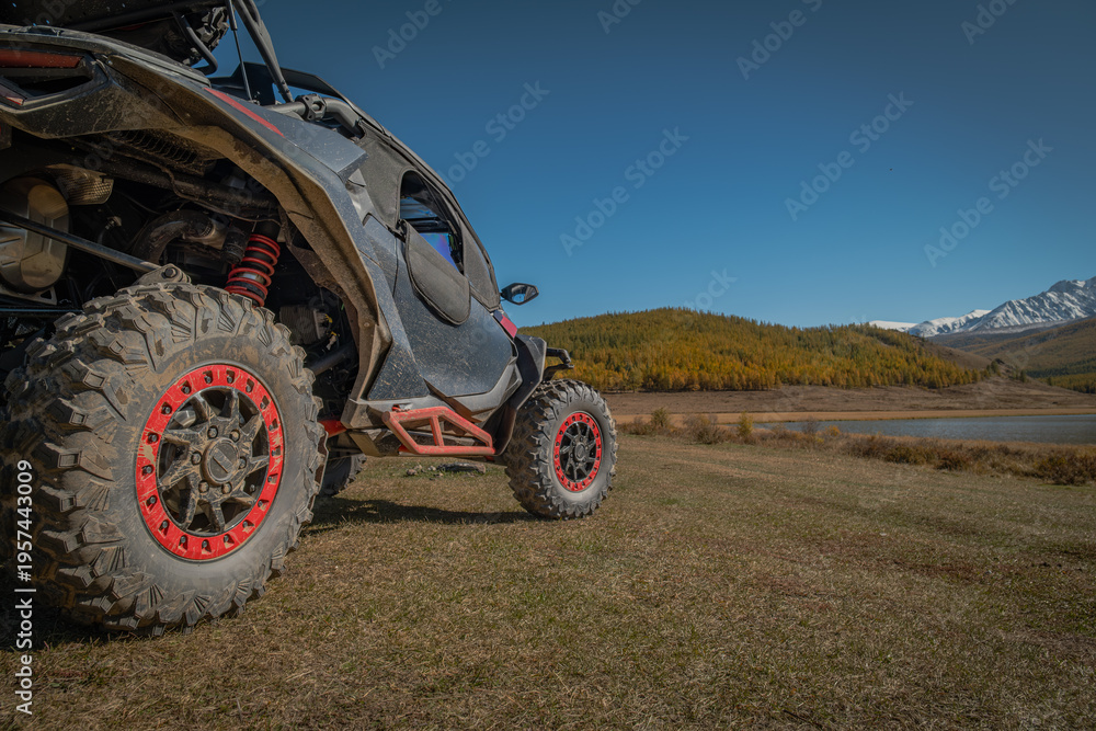 Obraz premium Close up of ATV off-road vehicle wheels with red beadlocks parked on mountain meadow by the lake at sunny autumn day.