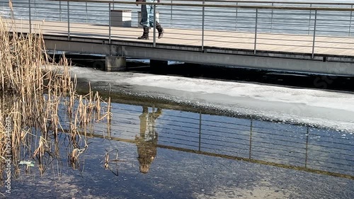 Person walking on lakeside boardwalk above icy water, calm reflection and spring thaw scene, slow living, mindfulness and connection with nature concept, minimal seasonal outdoor background