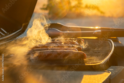 Grilling sausages at sunset in an outdoor setting with warm light and smoke rising from the barbecue