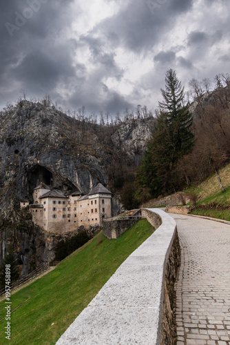 Predjama Castle in Slovenia with winding path leading to dramatic cave castle under cloudy sky