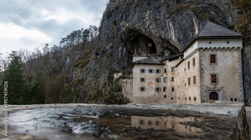 Predjama Castle in Slovenia with cave entrance and reflection in foreground under moody sky