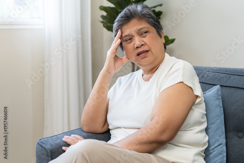 Unhappy asian elderly woman sitting on sofa at home, sick and stress headache feeling depressed suffering trauma from problem trouble tension, old tired difficulty mental health, senior exhausted pain