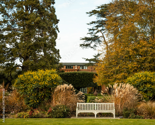 Obraz na plátně White wooden bench sitting in a formal garden featuring autumn foliage, ornament