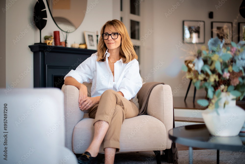 Obraz premium Blond haired smiling woman relaxing in an armchair in her modern home